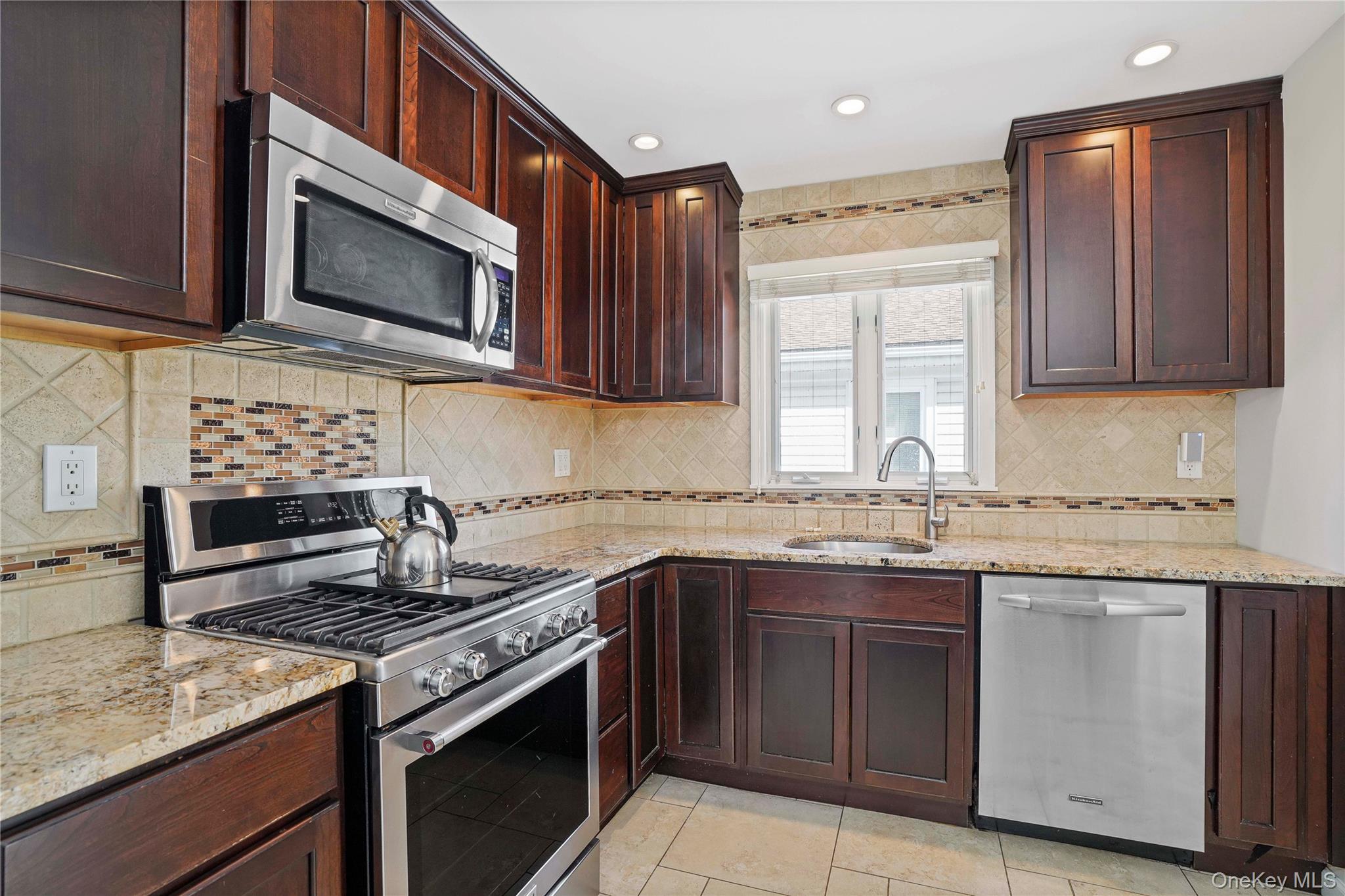 91-03 156th Avenue Queens, NY 11414 - Photo 14 of 50 Kitchen with appliances with stainless steel finishes, light stone countertops, backsplash, dark brown cabinetry, and recessed lighting