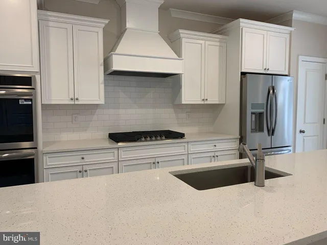 a kitchen with stainless steel appliances a stove a refrigerator a sink and white cabinets