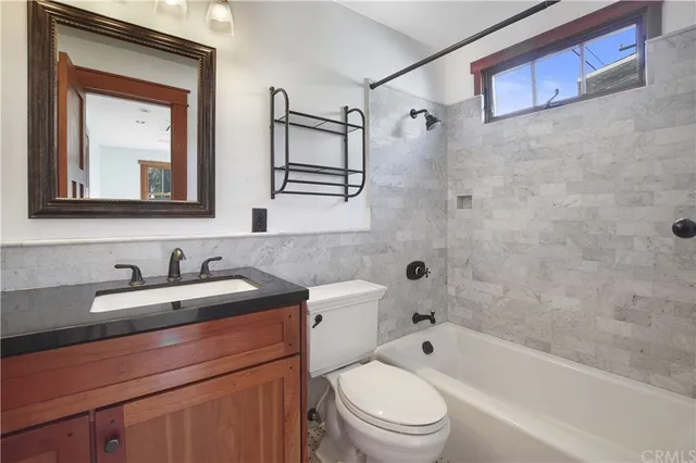 a bathroom with a granite countertop sink a toilet a mirror a vanity a bathtub and shower
