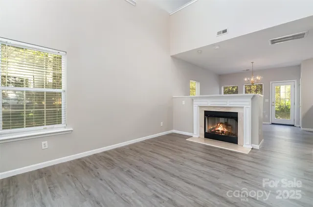 a view of an empty room with wooden floor fireplace and a window