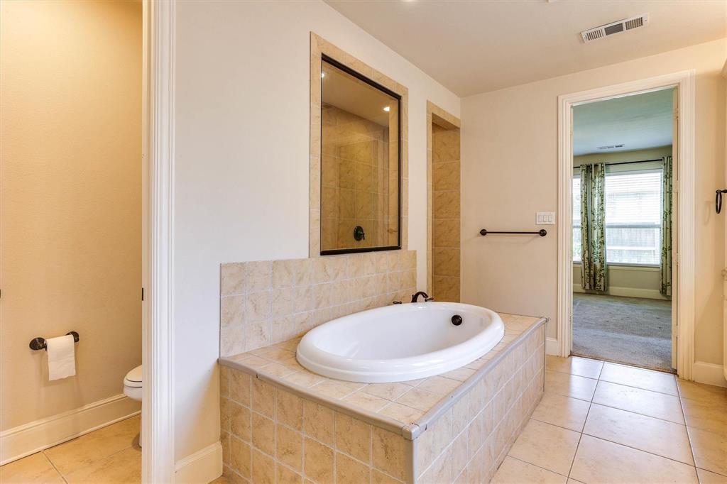 419 Rio Grande Drive Irving, TX 75039 - Photo 18 of 29 Soaking tub with surrounding tilework, complemented by tiled flooring and a separate shower enclosure with a dark-framed glass panel
