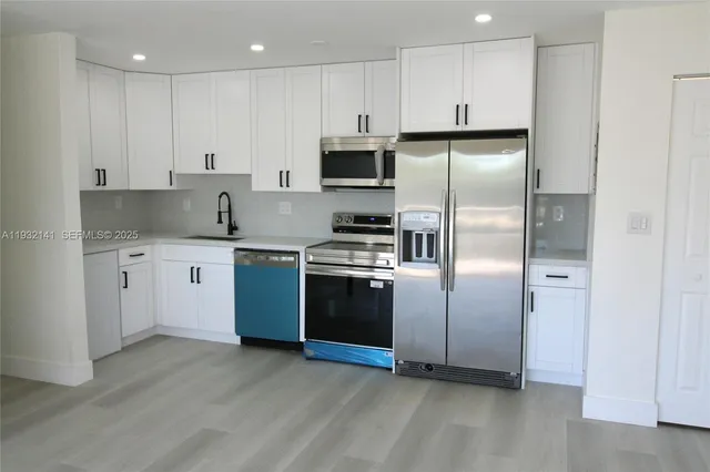 a kitchen with stainless steel appliances granite countertop a refrigerator a sink and white cabinets