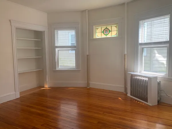 an empty room with wooden floor closet and windows