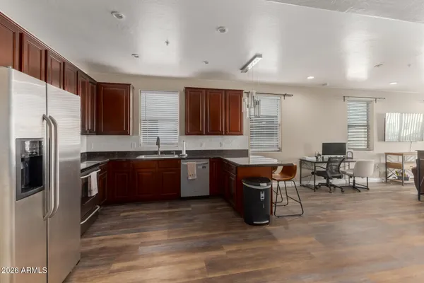 a kitchen with stainless steel appliances granite countertop a refrigerator a sink dishwasher a stove and a dining table with wooden floor