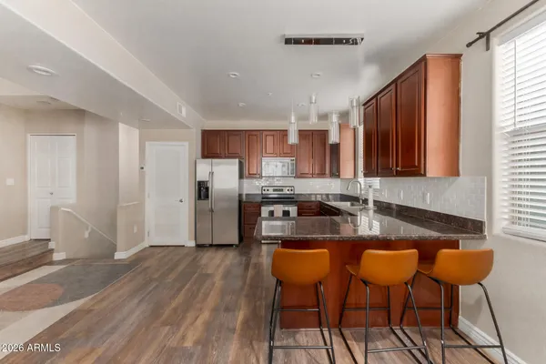 a kitchen with stainless steel appliances granite countertop a stove top oven a refrigerator a sink with white cabinets and wooden floor