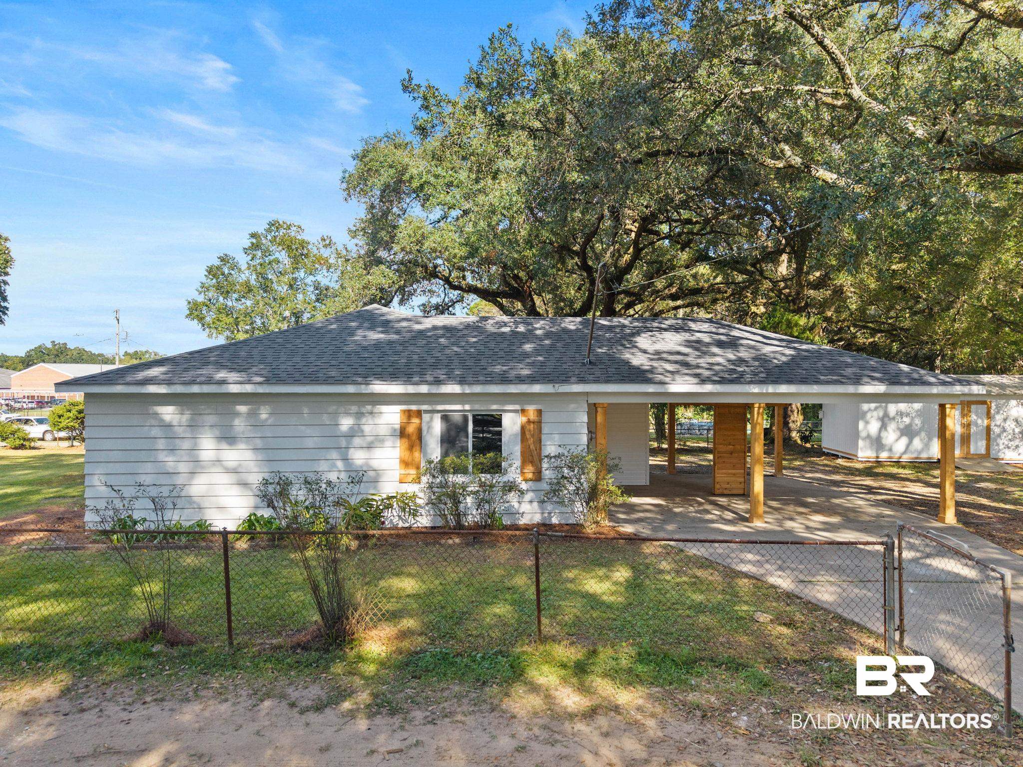 618 Pine Street Saraland, AL 36571 - Photo 2 of 41 Single story home featuring a shingled roof, an attached carport, a fenced front yard, and driveway