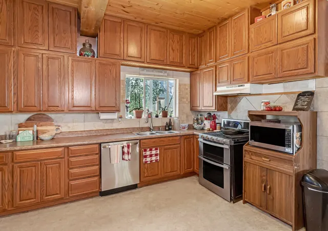 a large kitchen with stainless steel appliances granite countertop a refrigerator a sink dishwasher a stove and a refrigerator with wooden cabinets