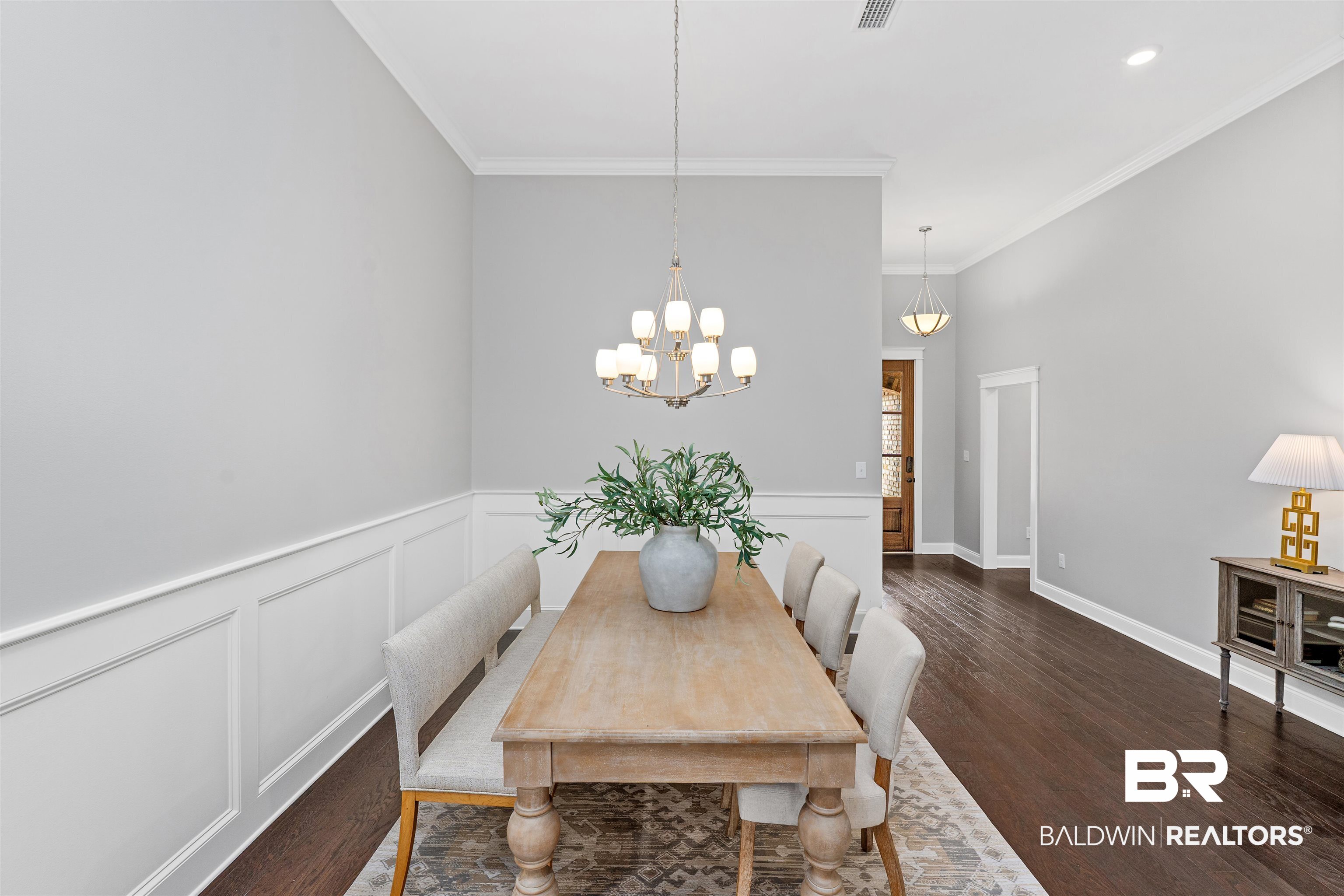 24838 Slater Mill Road Daphne, AL 36526 - Photo 12 of 46 Dining room featuring a wainscoted wall, crown molding, a decorative wall, a chandelier, and dark wood finished floors
