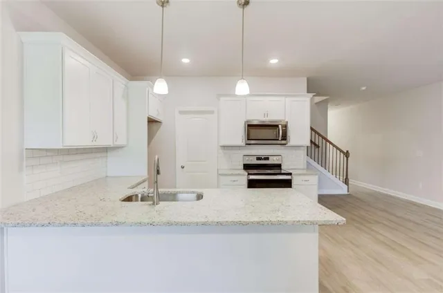 a kitchen with stainless steel appliances granite countertop a sink a stove and white cabinets with wooden floor