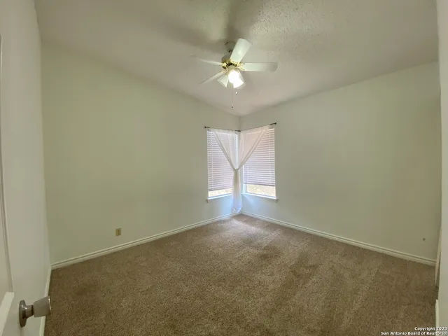 an empty room with a chandelier fan and windows