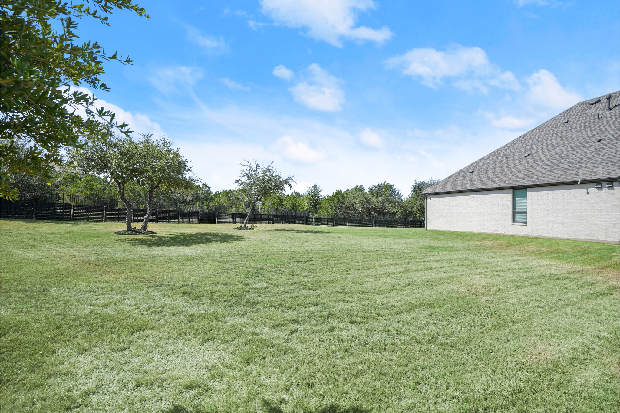 154 LITTLE Strm Cove Austin, TX 78737 - Photo 33 of 37 An expansive green lawn stretches across the fully fenced backyard beneath open blue skies.