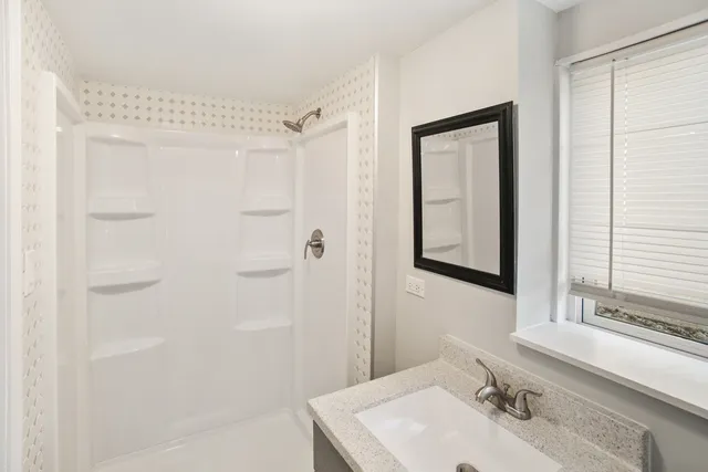 a bathroom with a granite countertop sink a mirror and shower