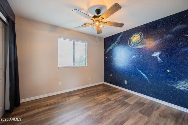 an empty room with a chandelier fan and wooden floor