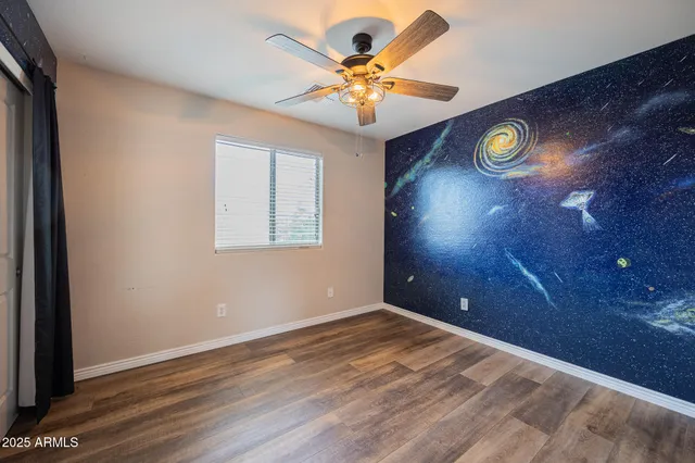 an empty room with a chandelier fan and wooden floor