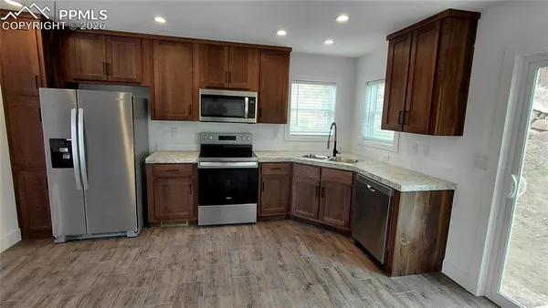 a kitchen with stainless steel appliances granite countertop a refrigerator a stove a sink a dining table and chairs with wooden floor