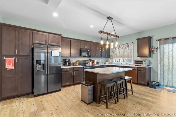a kitchen with stainless steel appliances granite countertop a refrigerator a sink dishwasher a stove and a dining table with wooden floor