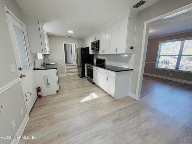 a kitchen with stainless steel appliances a stove top oven a sink a refrigerator white cabinets and wooden floor