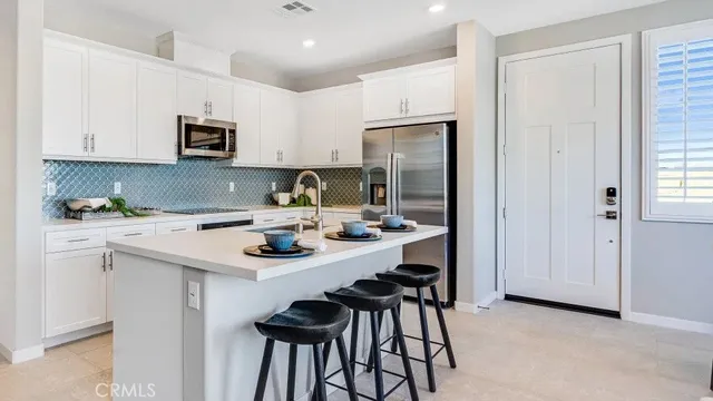 a kitchen with stainless steel appliances a sink a stove a refrigerator and white cabinets with wooden floor