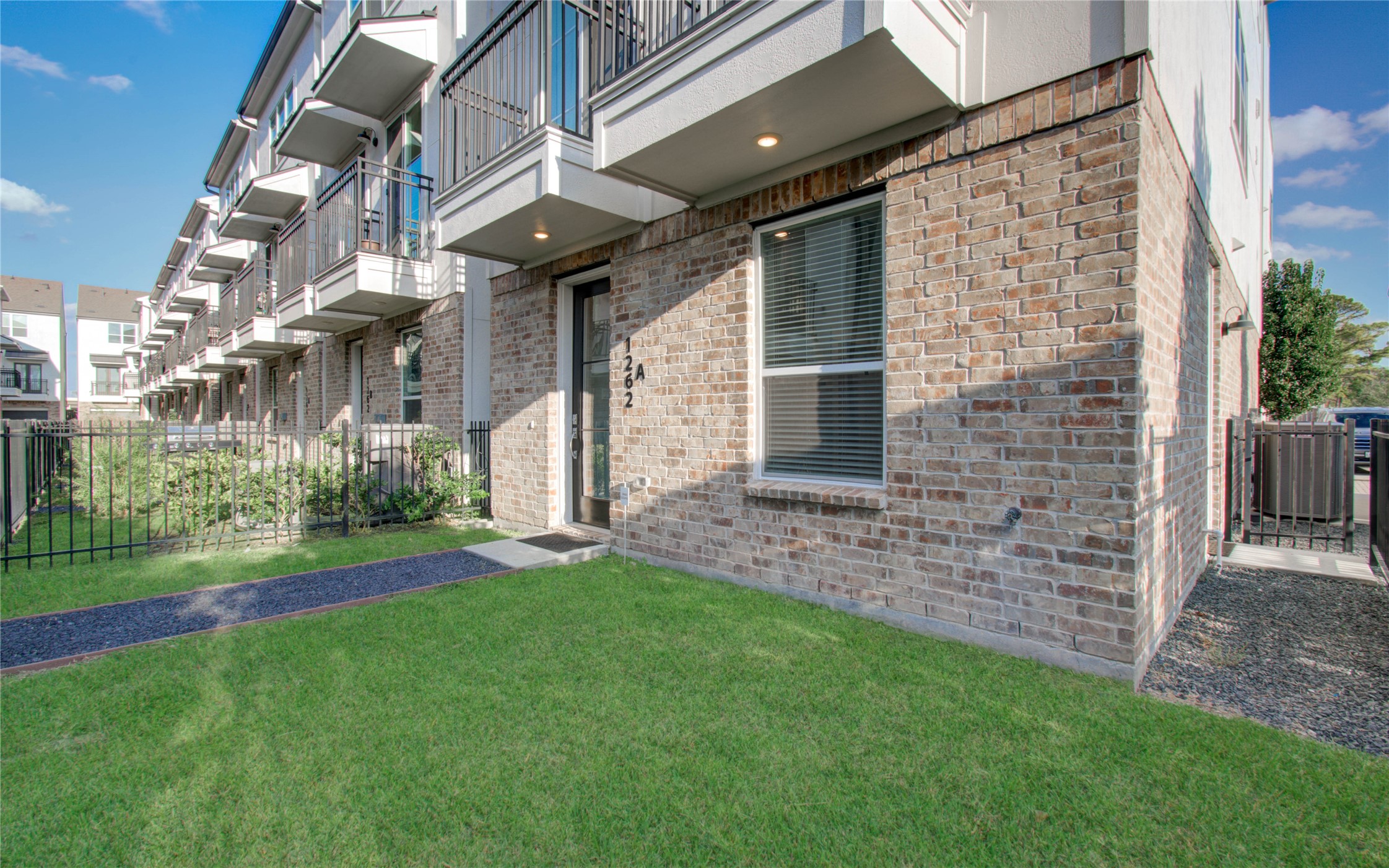 1262 North Post Oak Road, Unit A Houston, TX 77055 - Photo 6 of 50 This ground-level perspective emphasizes the rich brick texture of the lower floor and the spaciousness of the private lawn. Looking down the row, the upper-level overhangs and balcony structures create depth along the building's facade.