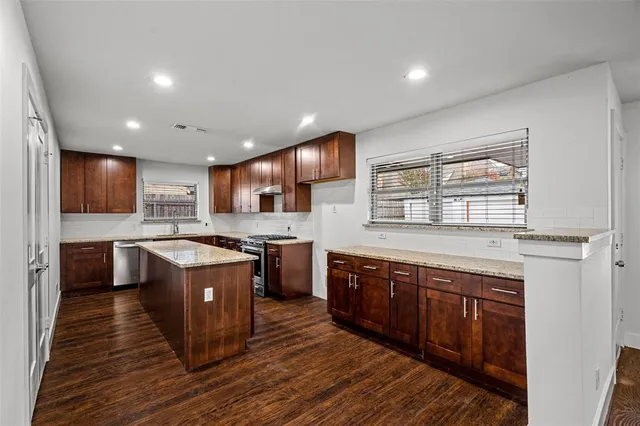 a large kitchen with stainless steel appliances granite countertop a stove a sink dishwasher a microwave oven and a refrigerator with wooden cabinets