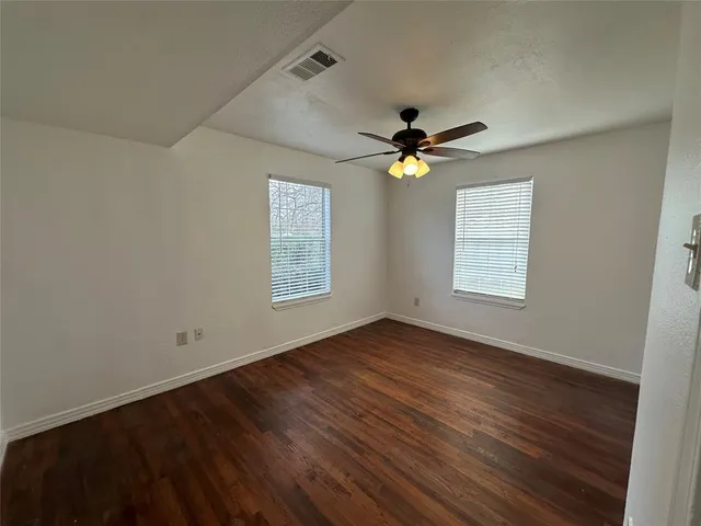 an empty room with wooden floor fan and windows