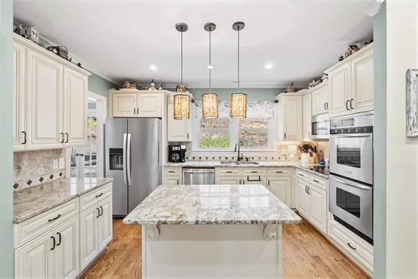a kitchen with stainless steel appliances granite countertop a refrigerator a stove a sink and white cabinets with wooden floor
