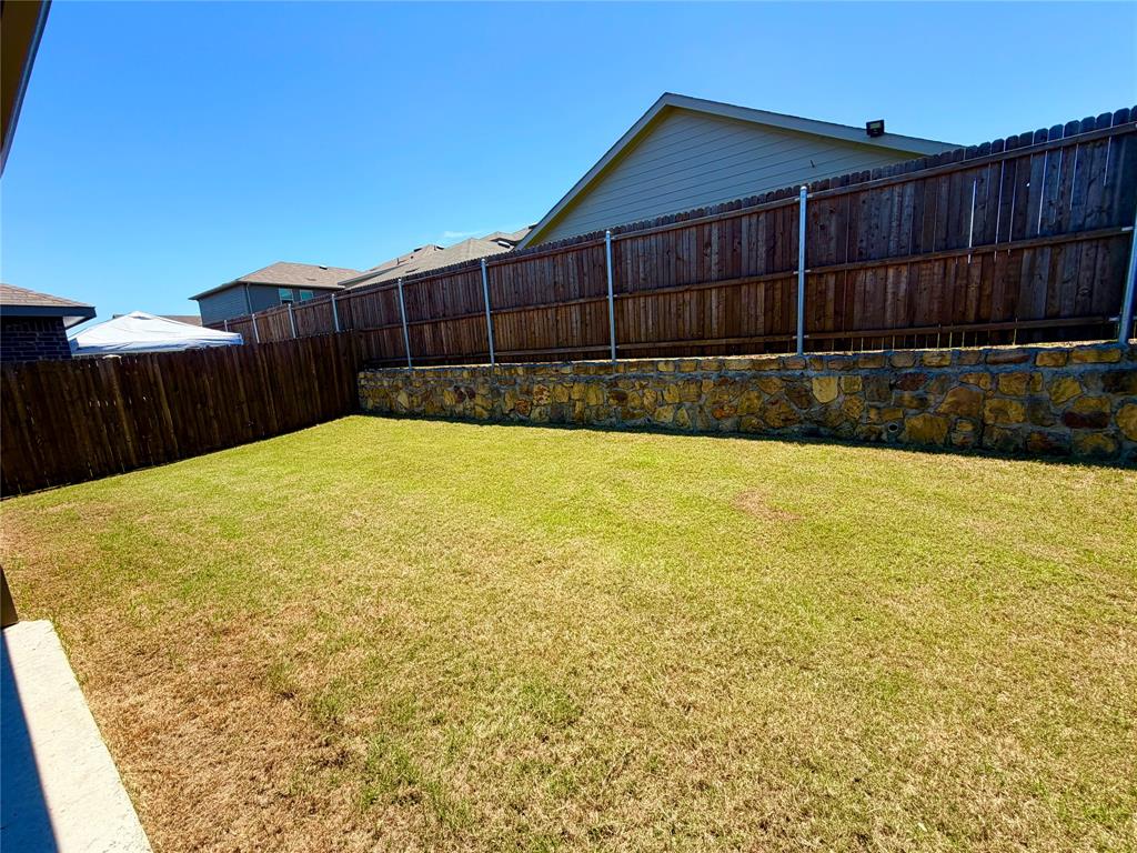 816 Country Road Royse City, TX 75189 - Photo 16 of 24 Spacious backyard featuring a stone retaining wall, wood fencing, and a large grass lawn
