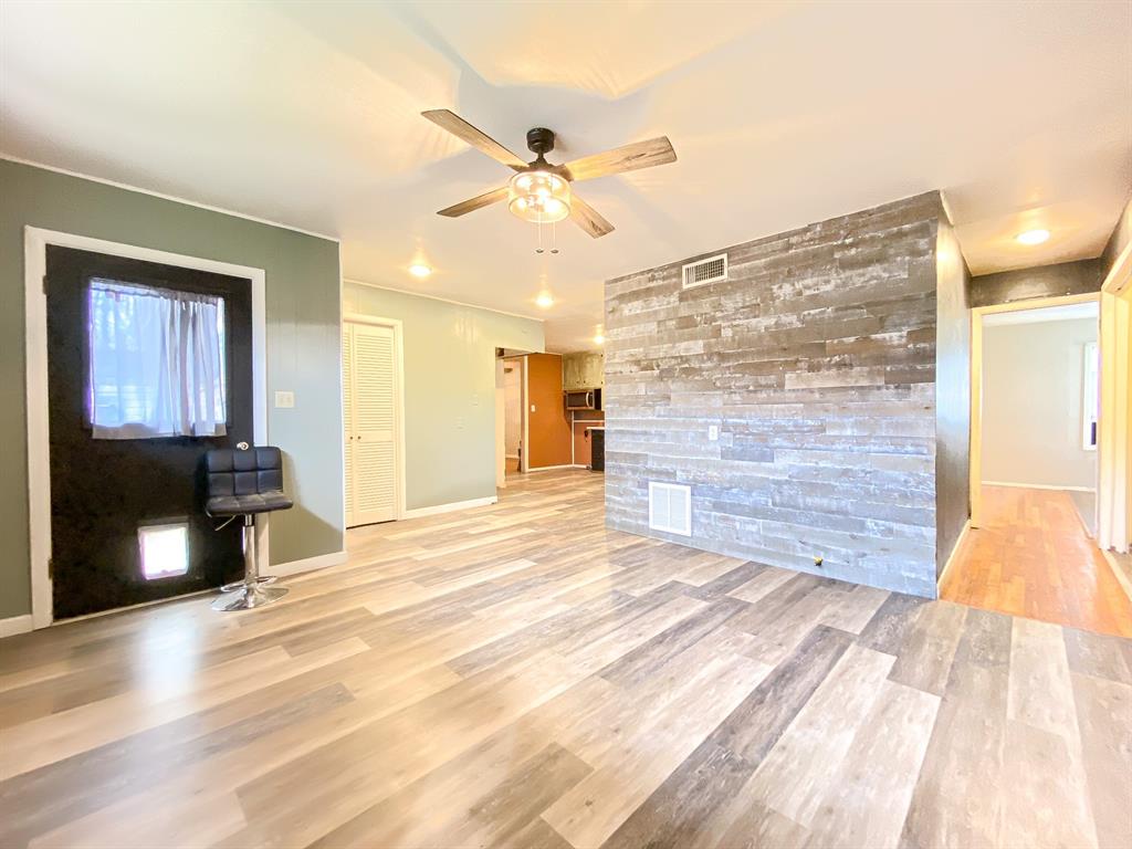 211 Paloma Street Winters, TX 79567 - Photo 7 of 19 a view of an empty room and kitchen with wooden floor and fan