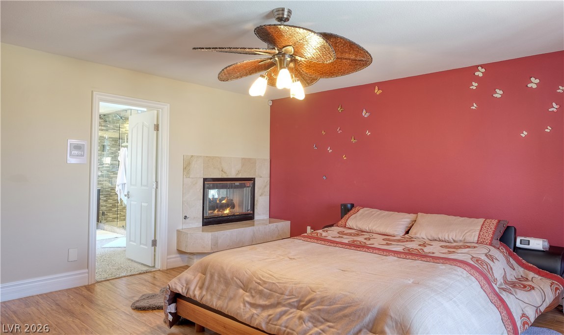 3704 North Campbell Road Las Vegas, NV 89129 - Photo 35 of 46 A cozy bedroom with a built-in fireplace and warm wooden floors, offering direct access to a private bathroom.