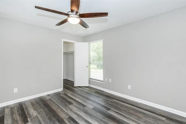 an empty room with wooden floor fan and windows