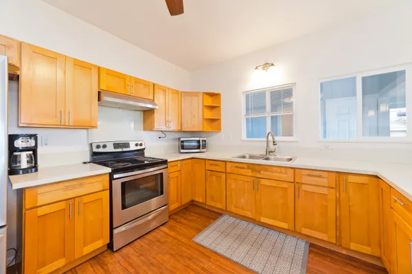 a kitchen with stainless steel appliances granite countertop wooden cabinets a sink a stove a dining table and chairs with wooden floor