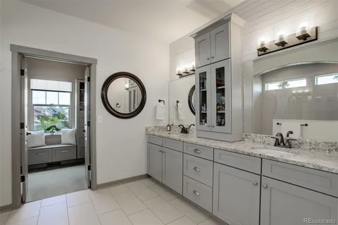 a bathroom with a granite countertop double vanity sink a two mirror a lamp a vanity a window and a glass door