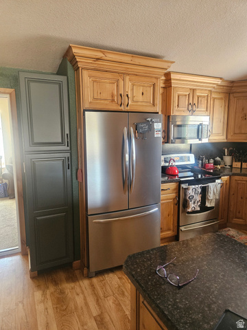 45758 Colt Road Fruitland, UT 84027 - Photo 10 of 21 Kitchen featuring wood-finish cabinetry with crown molding, dark granite-style countertops, wood-finish flooring, a stainless steel refrigerator, and a stainless steel range with overhead microwave