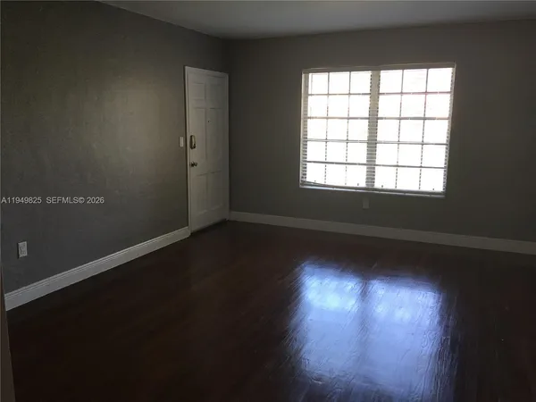 an empty room with wooden floor and windows with curtains