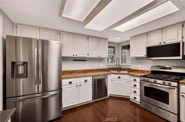 a kitchen with stainless steel appliances a stove top oven a sink a refrigerator white cabinets and wooden floor