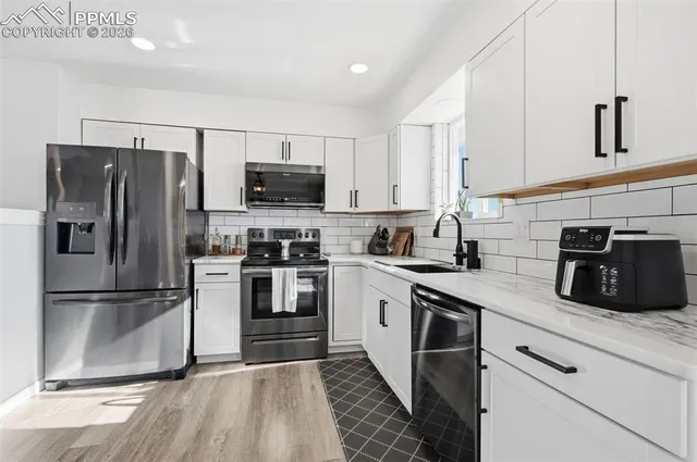 a kitchen with stainless steel appliances granite countertop a refrigerator a stove a sink and white cabinets