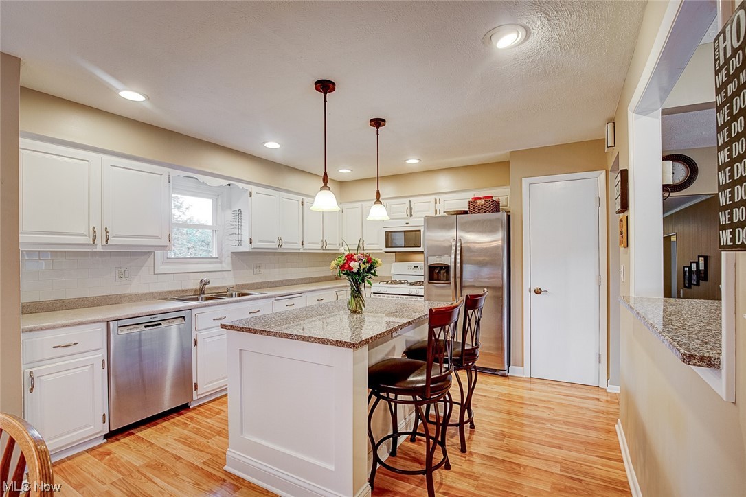 31950 Cannon Road Solon, OH 44139 - Photo 12 of 33 Kitchen featuring decorative light fixtures, backsplash, white cabinets, a kitchen island, light hardwood floors, appliances with stainless steel finishes, and light stone counters