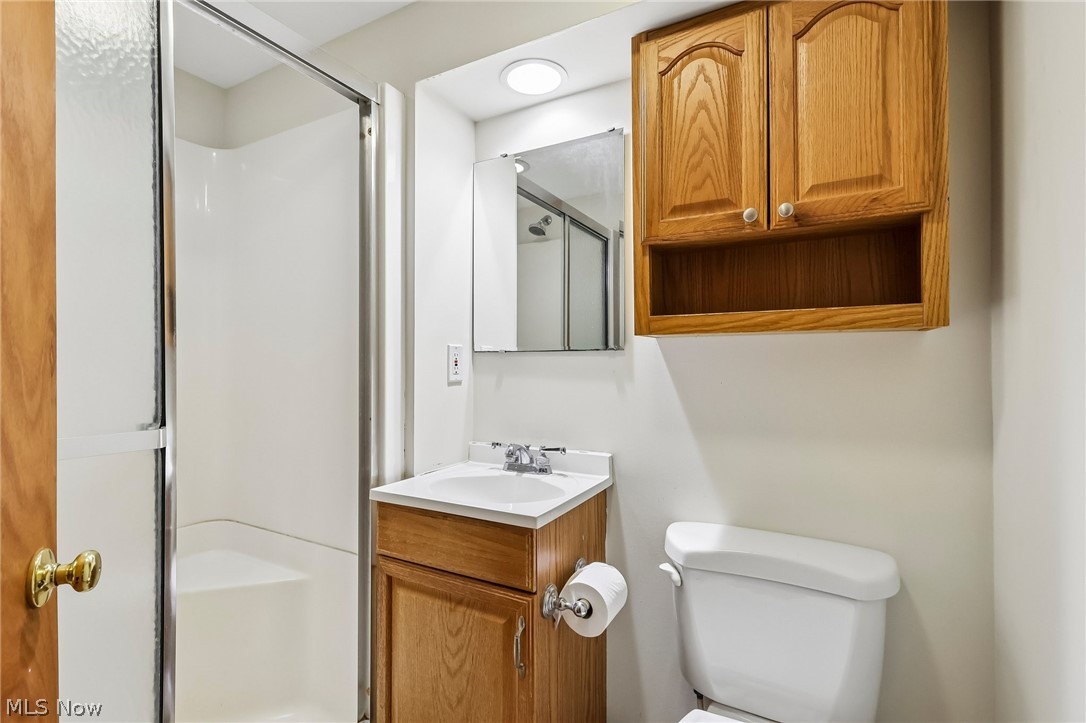 1638 South Cleveland Massillon Road Akron, OH 44321 - Photo 26 of 37 Bathroom featuring a standing shower with a clear glass enclosure, a vanity with a white countertop and wood-finish cabinetry, a wall-mounted medicine cabinet, and an overhead wood-finish cabinet
