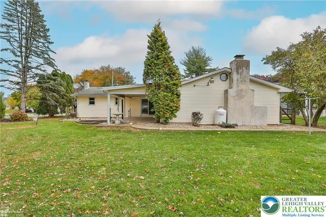 a view of a white house with a yard and table and chairs under an umbrella