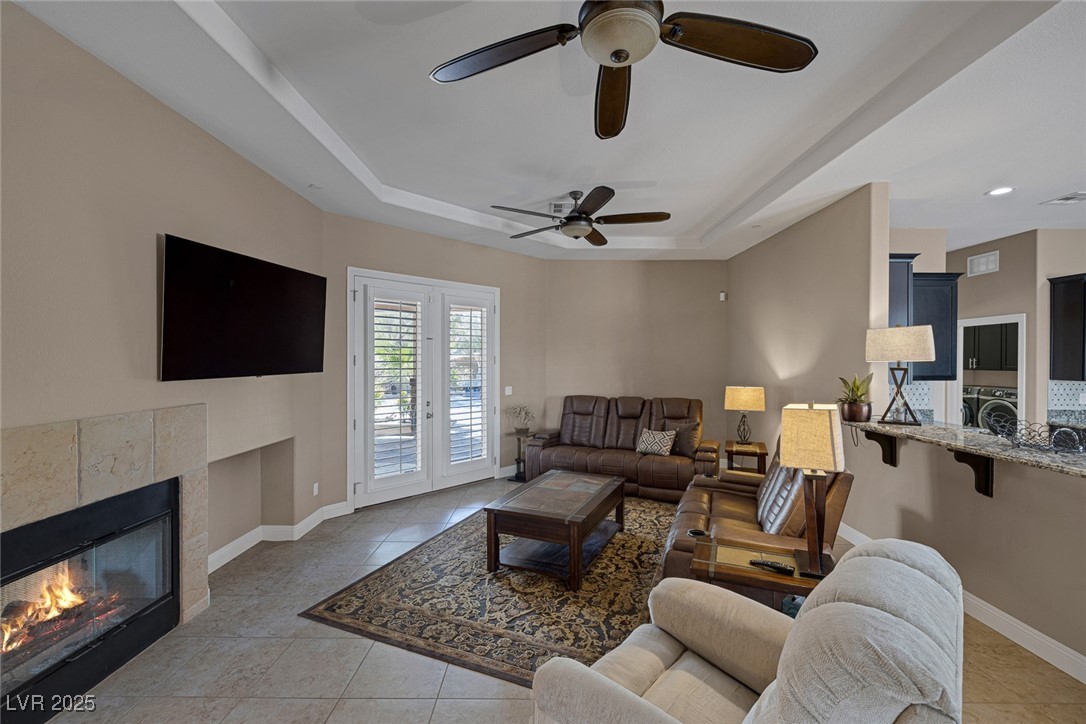 7687 West Pebble Road Las Vegas, NV 89113 - Photo 14 of 79 Living area with washer / clothes dryer, a fireplace, light tile patterned floors, a tray ceiling, and ceiling fan