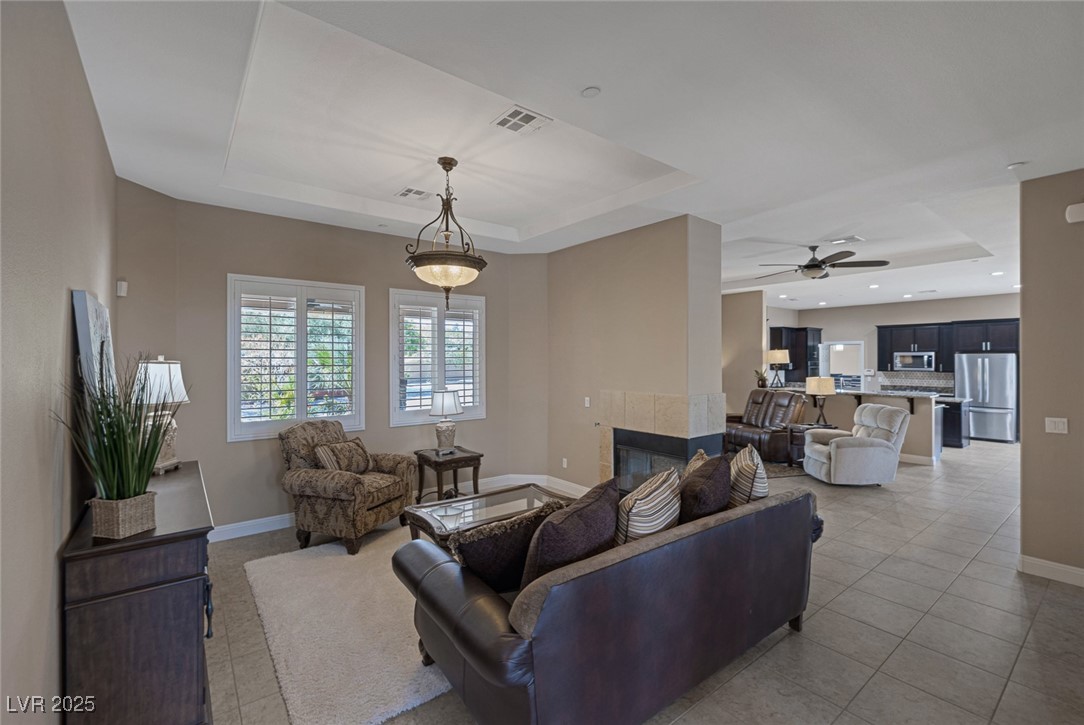 7687 West Pebble Road Las Vegas, NV 89113 - Photo 15 of 79 Living area with light tile patterned floors, a tray ceiling, a ceiling fan, visible vents, and baseboards