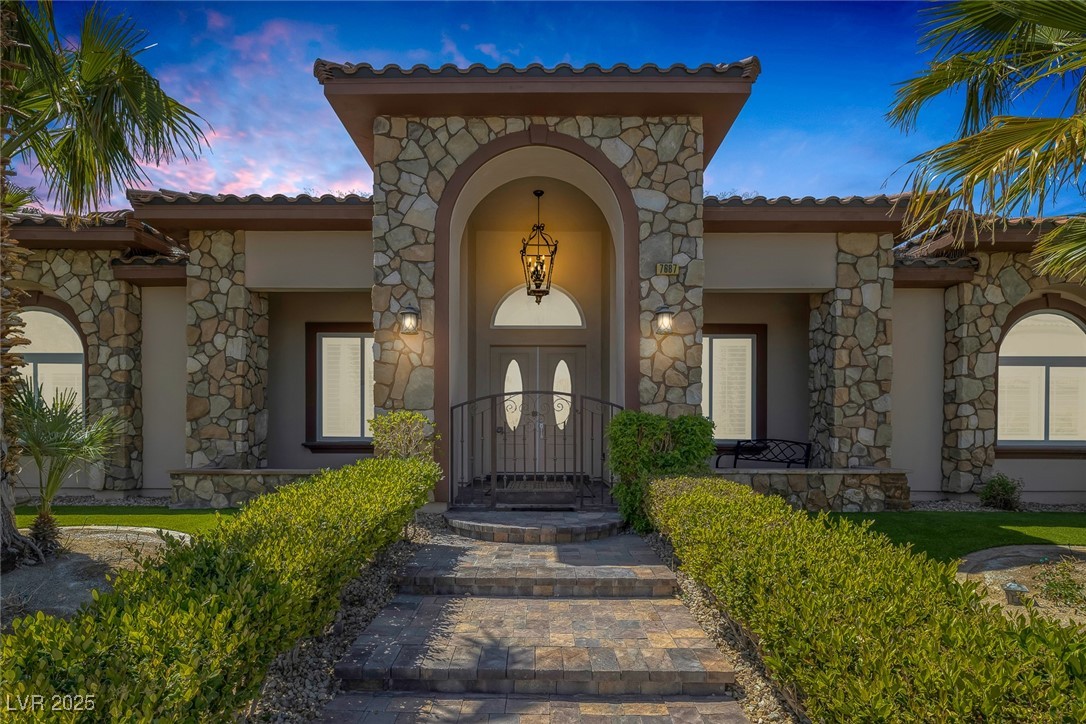 7687 West Pebble Road Las Vegas, NV 89113 - Photo 2 of 79 Exterior entry at dusk featuring covered porch, stucco siding, stone siding, and a tile roof