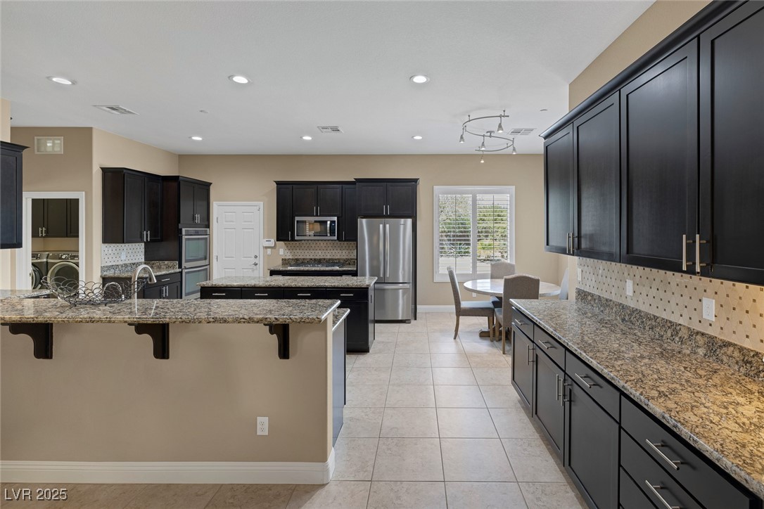 7687 West Pebble Road Las Vegas, NV 89113 - Photo 21 of 79 Kitchen with a center island, light stone countertops, a breakfast bar area, decorative backsplash, and stainless steel appliances