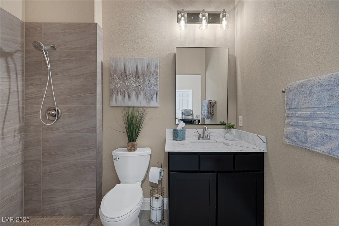 7687 West Pebble Road Las Vegas, NV 89113 - Photo 32 of 79 Bathroom featuring toilet, a tile shower, vanity, and a textured wall
