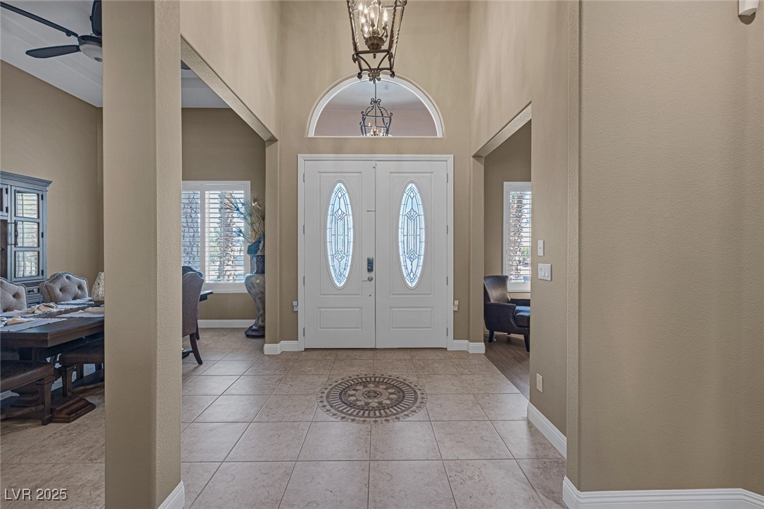 7687 West Pebble Road Las Vegas, NV 89113 - Photo 7 of 79 Foyer entrance with light tile patterned floors, baseboards, a high ceiling, and ceiling fan with notable chandelier