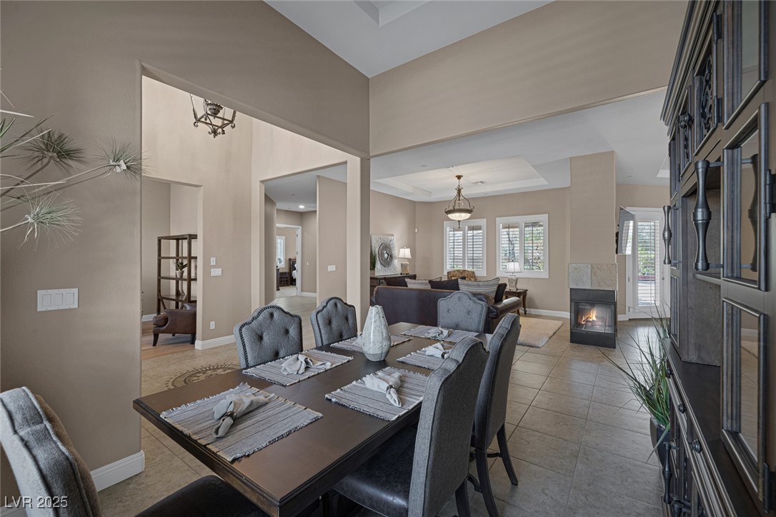7687 West Pebble Road Las Vegas, NV 89113 - Photo 10 of 79 Tiled dining area featuring a tiled fireplace, a high ceiling, baseboards, and a raised ceiling
