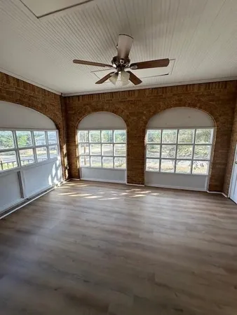 an empty room with wooden floor fan and windows