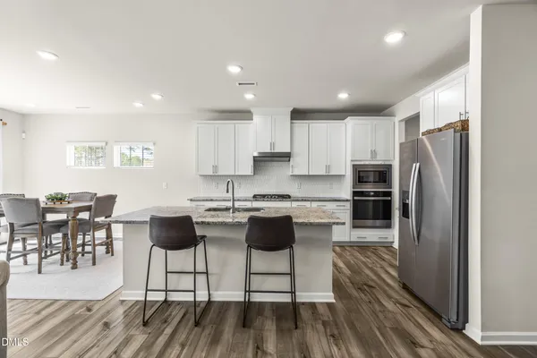 a kitchen with stainless steel appliances kitchen island granite countertop a refrigerator a stove a sink a dining table and chairs with wooden floor