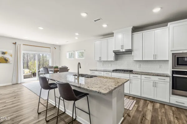 a kitchen with stainless steel appliances granite countertop a stove top oven a sink a refrigerator and white cabinets with wooden floor