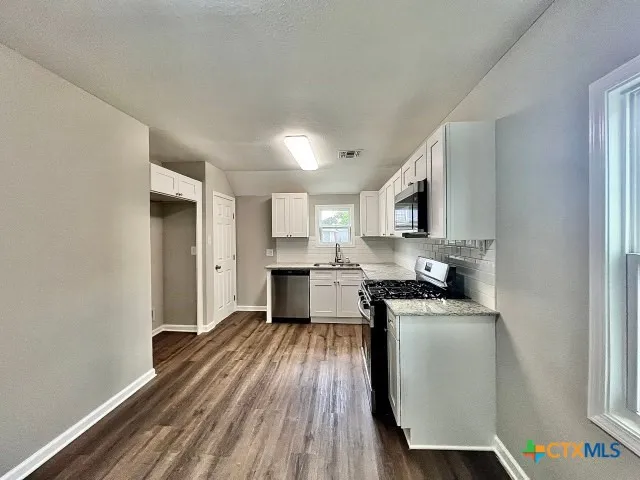 a kitchen with granite countertop a sink cabinets stainless steel appliances and a window